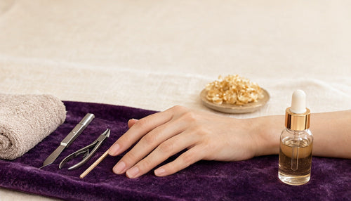Cuticle pusher, nippers and cuticle oil beside a hand with clean natural nails