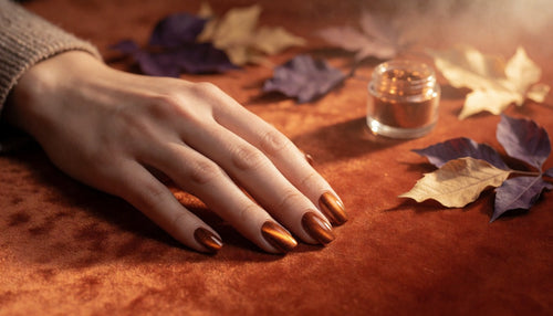 Hand displaying chrome and cat-eye nail finishes styled with fall leaves and warm lighting