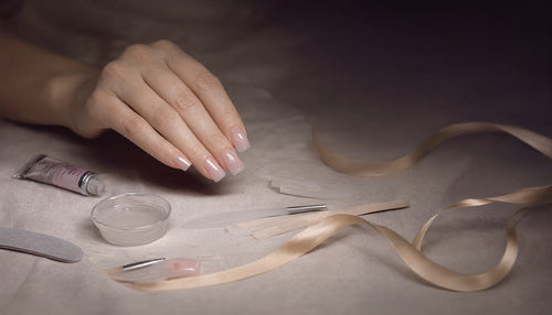 Poly gel nail extension tools and finished pink nails laid out on linen