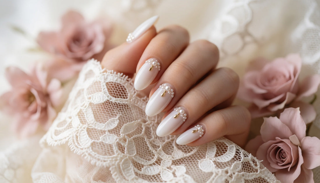 Hand with soft white bridal nails featuring pearl clusters and a delicate gold charm